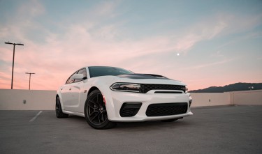 WHITE DODGE CHARGER SRT HELLCAT WIDEBODY ON THE TOP FLOOR OF THE PARKING GARAGE AT DUSK