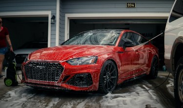 A RED CAR BEING WASHED BY A GARAGE 