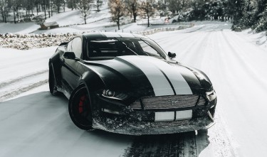 A BLACK AND WHITE FORD SHELBY MUSTANG ON SNOW COVERED ROAD 